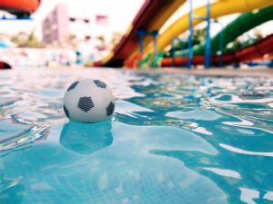 A vibrant scene at a water park featuring a soccer ball floating in a pool with colorful slides in the background.